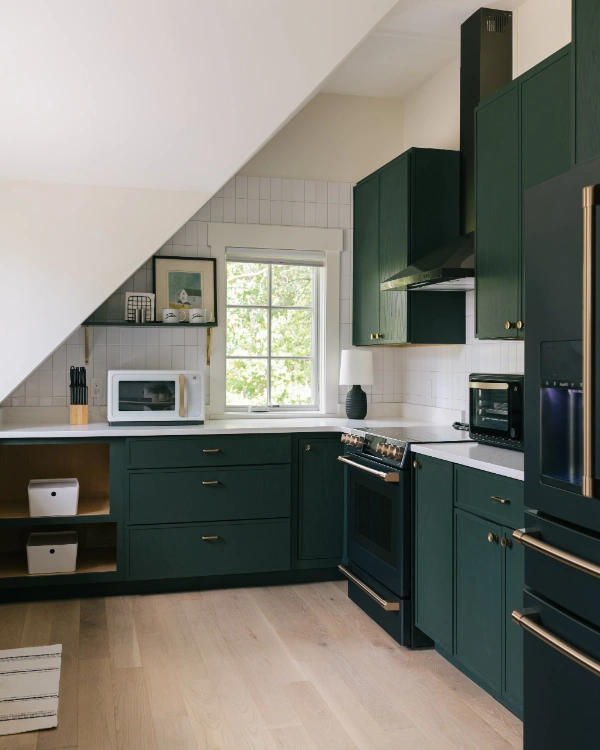 Compact kitchen corner with green cabinets, under-slope ceiling design, modern appliances, and white tile backsplash